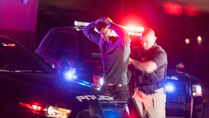 Man with his hands above his head while being arrested by a policeman