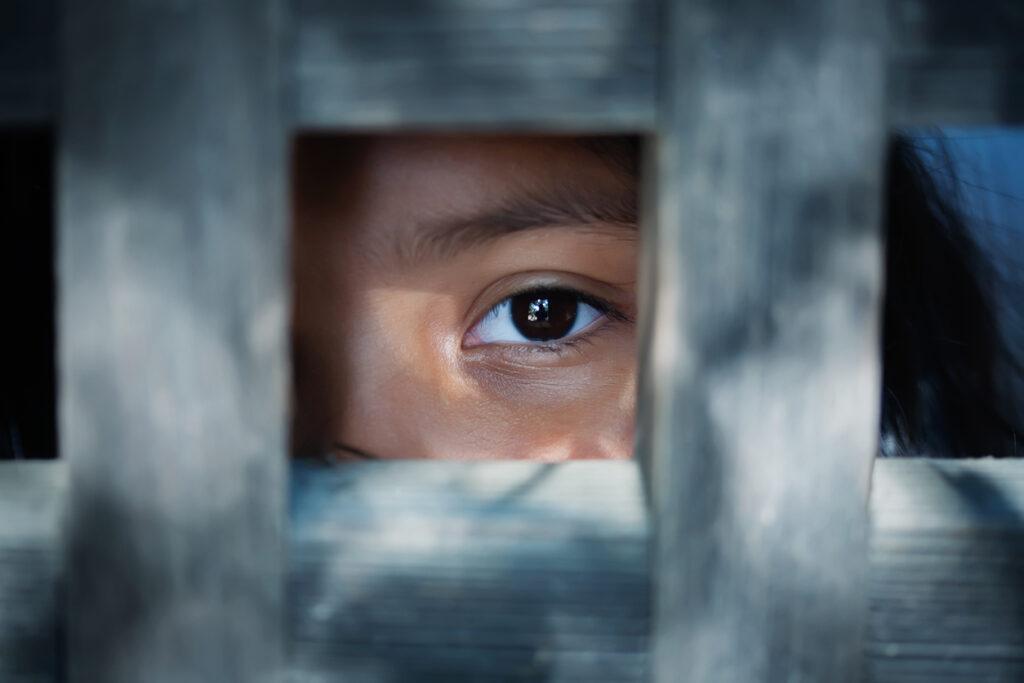 Blank stare of a child's eye who is standing behind a wooden frame.