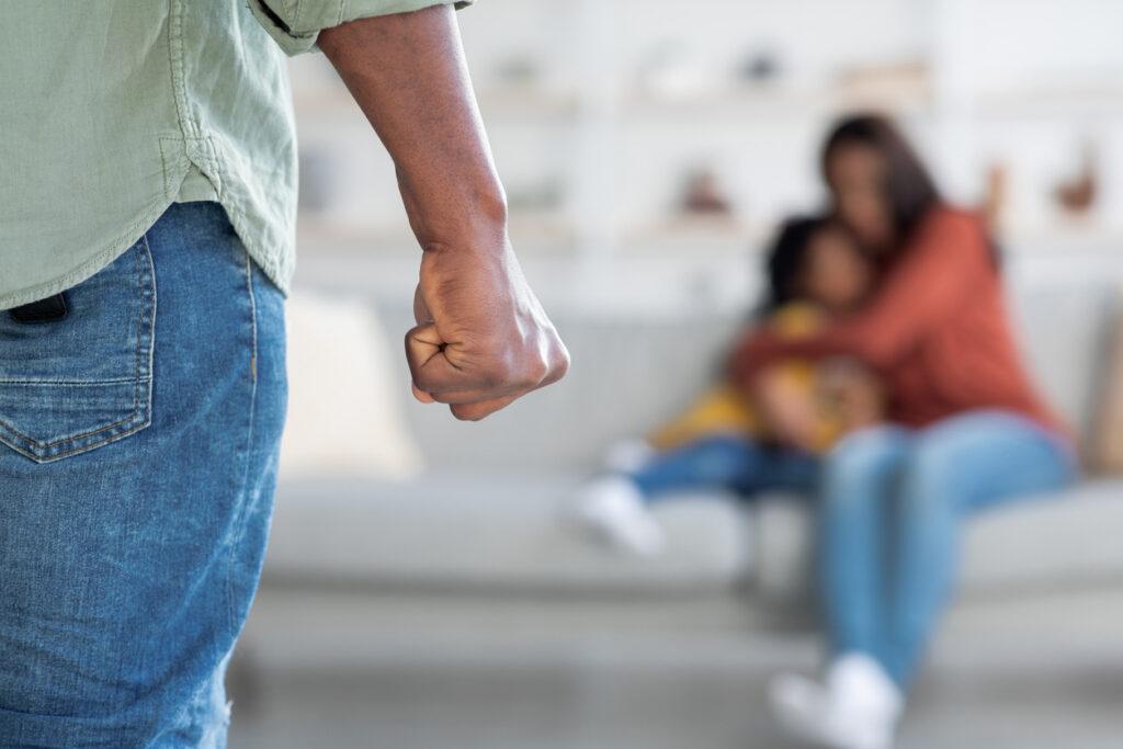A man threatening his scared wife and daughter from a distance with his fist. The image represents domestic violence.