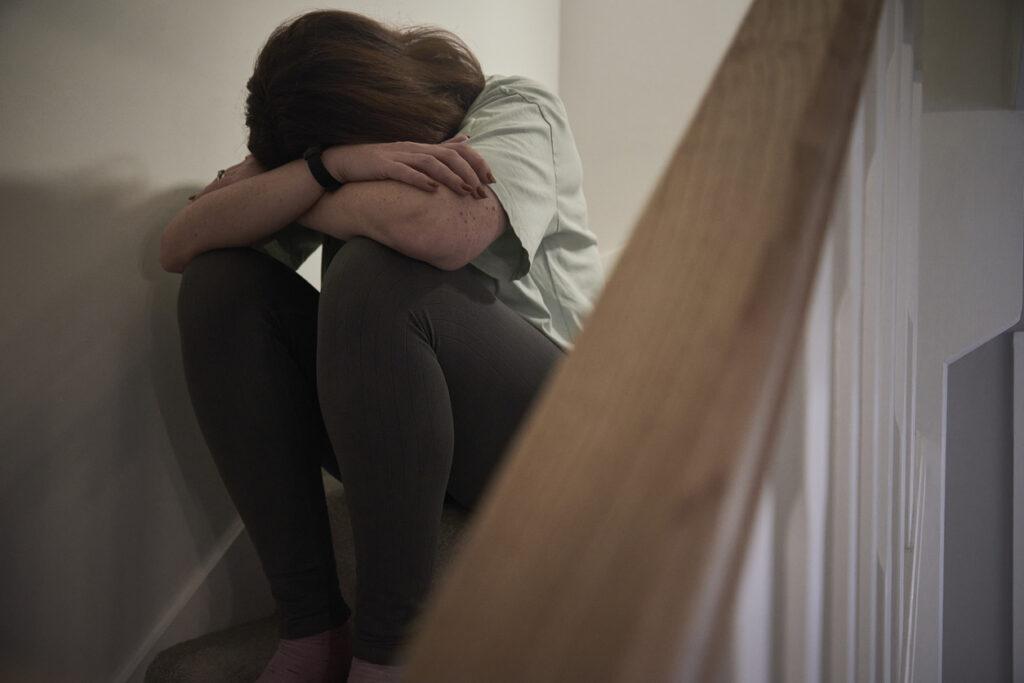 A woman crying while she's sitting on the stairs of her home.