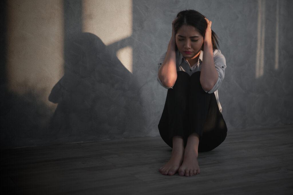 Woman sitting on the ground at home while holding her ears.