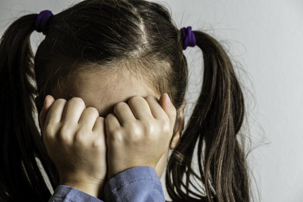 Young girl hiding her face with her hands.