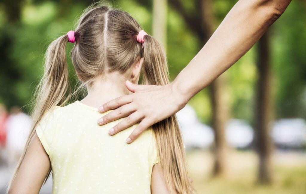 Adult hand supporting a young girl while walking to suggest outcry witness.