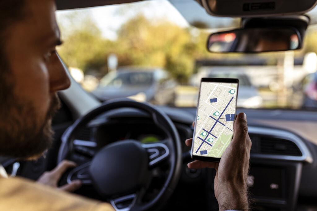 Man inside a car looking at a GPS tracker on his phone.