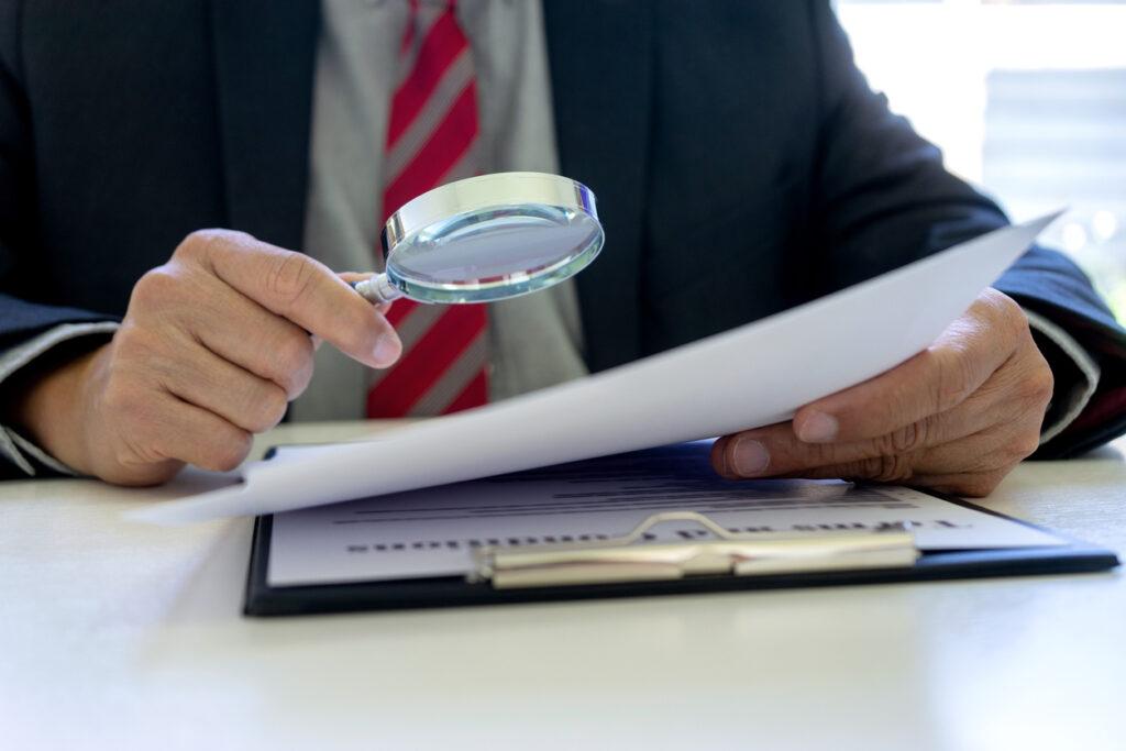 Man using a magnifying glass while studying documents.