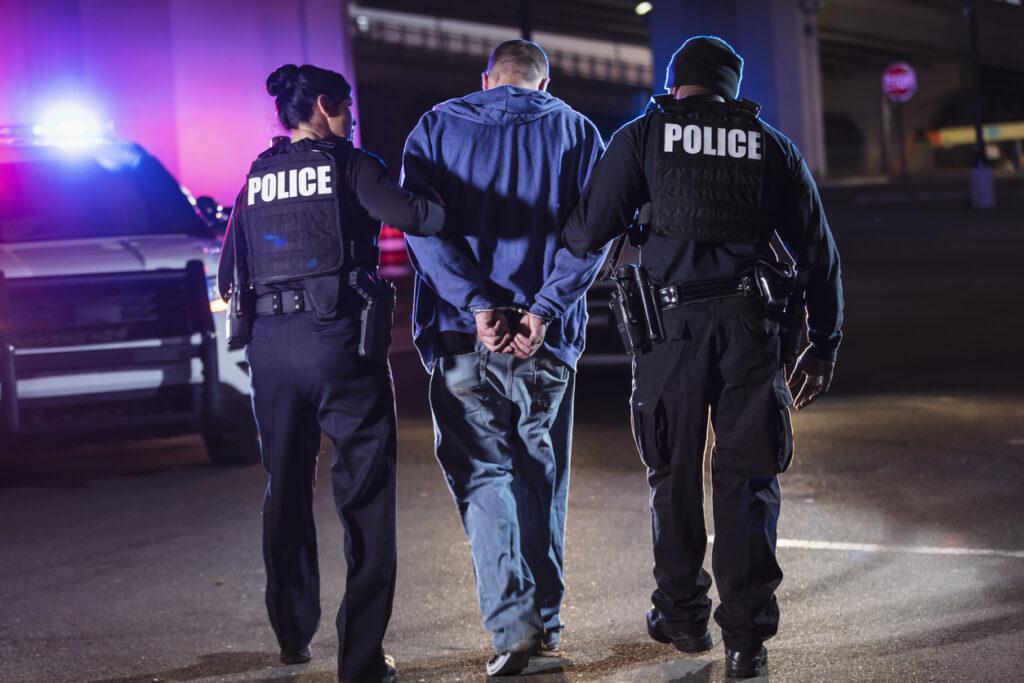 Police officers arresting a handcuffed man.